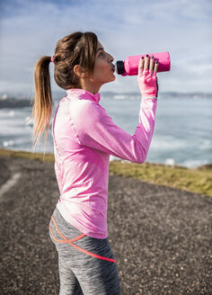 Spanien, Gijon, sportliche junge Frau, die an der Küste aus einer Wasserflasche trinkt - MGOF000094