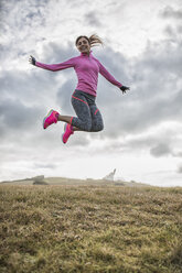 Spanien, Gijon, sportliche junge Frau springt auf Wiese - MGOF000103