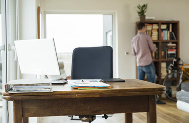 Empty desk with man in background at bookshelf - UUF003311