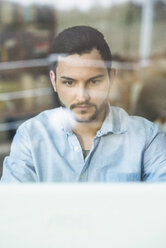 Young man behind windowpane working at computer - UUF003320