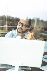 Young man behind windowpane working at computer - UUF003323