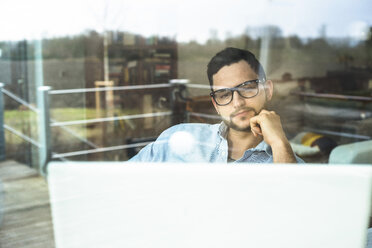 Young man behind windowpane working at computer - UUF003324