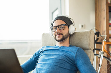 Young man using laptop and wearing headphones - UUF003342