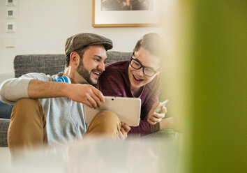 Zwei lachende junge Männer zu Hause mit digitalem Tablet und Mobiltelefon - UUF003352