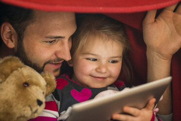 Father and daughter with digital tablet under blanket - UUF003357