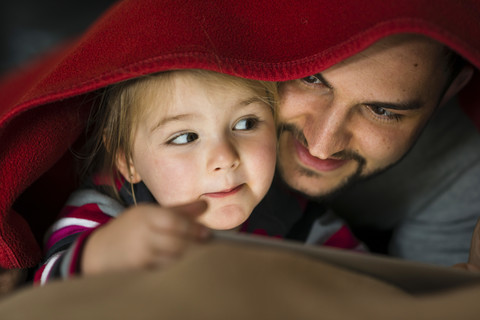 Vater und Tochter mit digitalem Tablet unter der Bettdecke, lizenzfreies Stockfoto