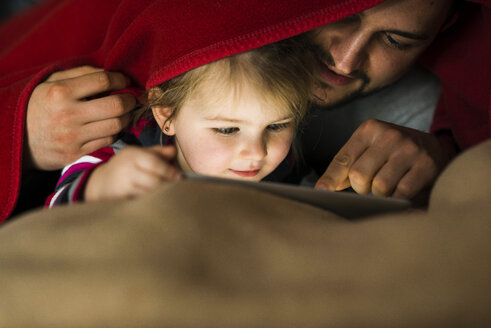 Vater und Tochter mit digitalem Tablet unter der Bettdecke - UUF003361