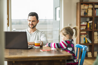 Vater und Tochter mit Laptop und Spiel am Holztisch - UUF003363