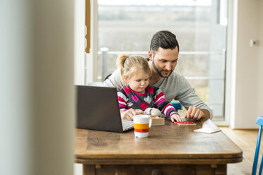 Vater und Tochter mit Laptop und Spiel am Holztisch - UUF003364