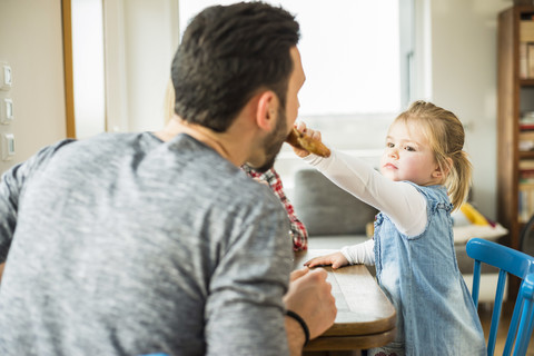 Tochter füttert Vater am Esstisch, lizenzfreies Stockfoto