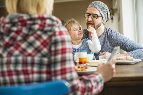 Tochter füttert Vater am Esstisch, lizenzfreies Stockfoto