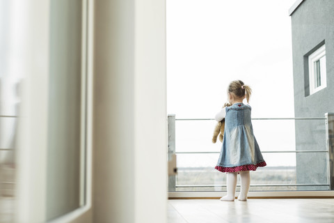 Girl holding teddy looking out of window stock photo