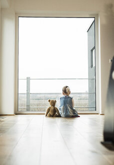 Mädchen sitzt neben Teddy und schaut aus dem Fenster - UUF003387