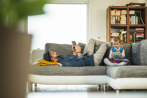 Vater und Tochter mit digitalem Tablet und Smartphone auf dem Sofa - UUF003389