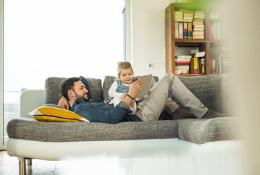 Vater und Tochter mit digitalem Tablet auf dem Sofa - UUF003390