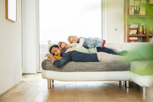 Family lying on couch on top of each other with closed eyes - UUF003392