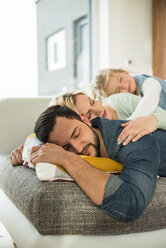 Family lying on couch on top of each other with closed eyes - UUF003402