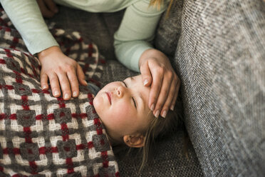 Mutter berührt die Stirn ihrer kranken Tochter, die auf der Couch liegt - UUF003393