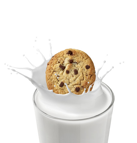 Schokoladenkeks, der in ein Glas Milch fällt, vor weißem Hintergrund, lizenzfreies Stockfoto