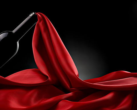 Wine bottle and flowing red silk in front of black background stock photo