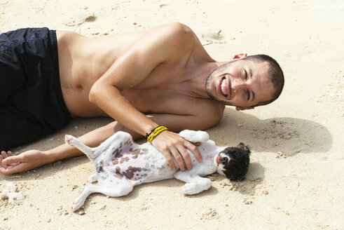 Philipinnes, Visayas, lächelnder Mann spielt mit einem Hund am Strand - GEMF000041
