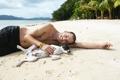 Philipinnes, Visayas, lächelnder Mann spielt mit einem Hund am Strand, lizenzfreies Stockfoto