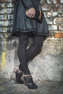 Woman leaning on brick wall holding leather handbag - DEGF000339
