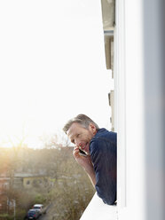 Germany, Cologne, Man leaning out of window using mobile phone - RHF000536