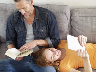 Älterer Mann mit erwachsener Tochter liest auf dem Sofa - RHF000505