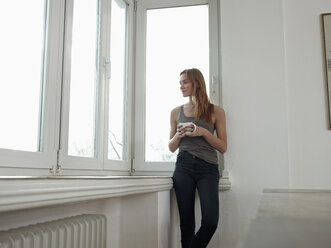 Germany, Cologne, Young woman standing at window, looking out - RHF000542