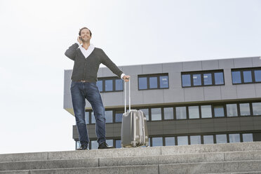 Telefonierender Geschäftsmann mit seinem Koffer auf der Treppe stehend - PDF000769