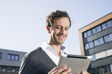 Porträt eines lächelnden Geschäftsmannes mit Blick auf ein digitales Tablet - PDF000778