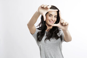 Portrait of smiling young woman building frame with her fingers - GDF000672