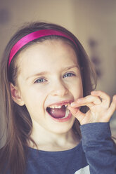 Porträt eines lächelnden kleinen Mädchens mit Zahnlücke, das einen Milchzahn in der Hand hält - SARF001348