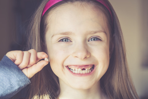 Portrait of smiling little girl with tooth gap holding milk tooth in her hand stock photo