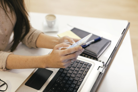 Junge Unternehmerin nutzt Smartphone im Home Office, lizenzfreies Stockfoto