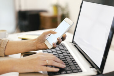 Young female entrepreneur using smartphone and laptop at home office - EBSF000441