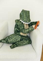 Kleiner Junge im Dinosaurierkostüm sitzt mit Smartphone auf der Couch - MFF001482