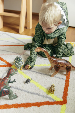 Kleiner Junge im Dinosaurierkostüm spielt mit Spielzeugdinosauriern, lizenzfreies Stockfoto