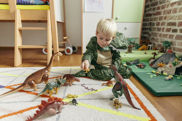 Little boy wearing dinosaur costume playing with toy dinosaurs - MFF001488