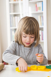 Little girl cutting out yellow modeling clay - LVF002849