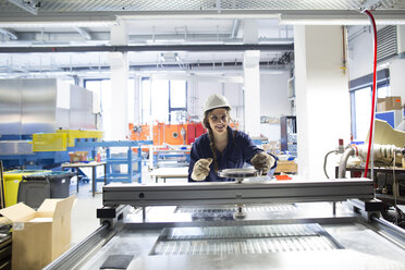 Smiling technician in factory hall adjusting plate - SGF001335