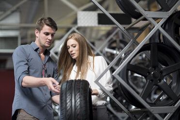 Shop assistant showing woman a tyre in tyre shop - ZEF004002