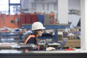 Techniker mit Warnweste in einer Fabrikhalle mit Laptop - SGF001340