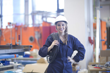 Lächelnder Techniker in einer Fabrikhalle mit Kabeln - SGF001342