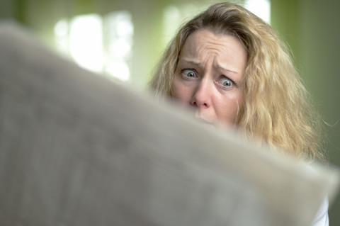 Verängstigte Frau liest Zeitung, lizenzfreies Stockfoto