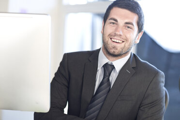 Portrait of smiling young businessman at desk in an office - ZEF003552