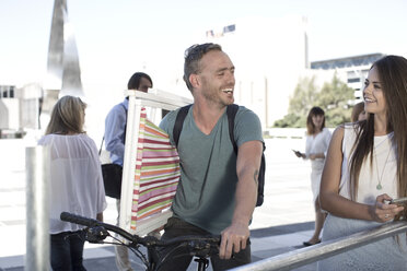 Man on bicycle carrying deck chair and talking to woman - ZEF004932