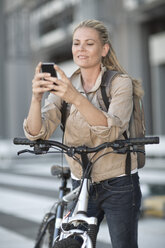 Blonde Frau auf dem Fahrrad mit Mobiltelefon - ZEF004943