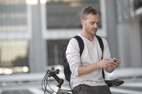 Blonder Mann auf dem Fahrrad mit Smartphone - ZEF004944